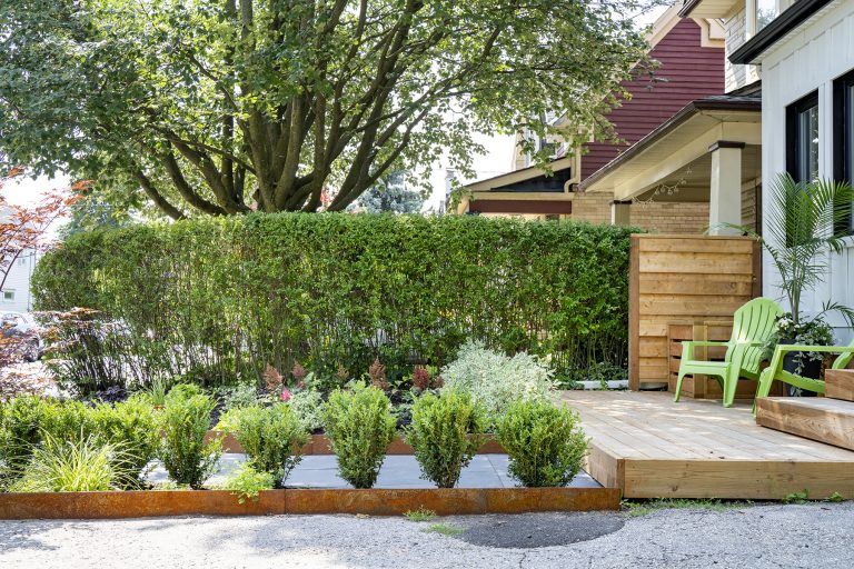 A beautiful garden by Earth and Sole Ltd, featuring a natural flagstone pathway leading to a wooden bench surrounded by lush perennial plants and trees, with a retaining wall in the background.