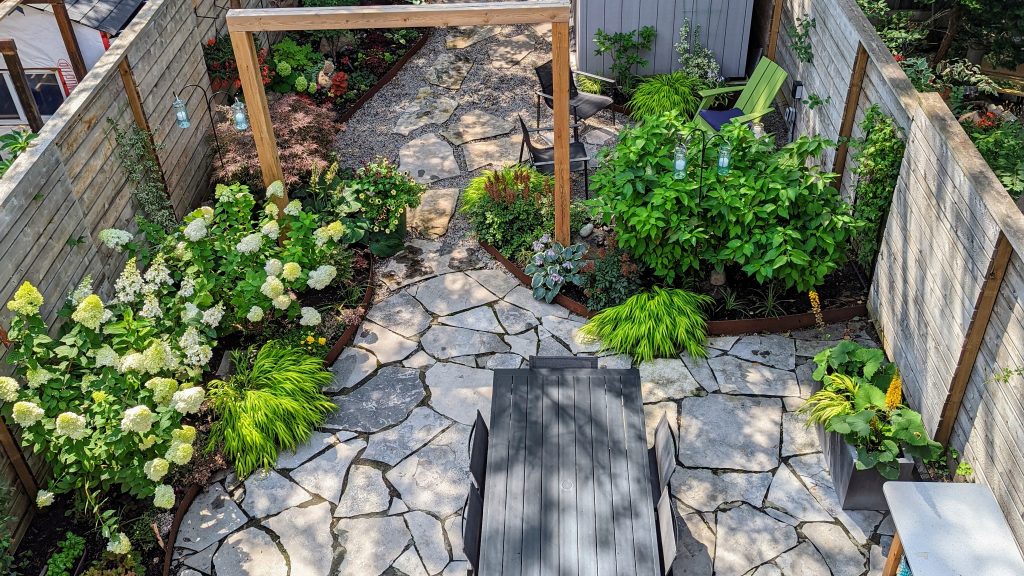 A lush and vibrant garden designed and maintained by Earth and Sole Ltd, featuring a variety of colorful flowers and greenery, including roses, hydrangeas, and hostas, set against a backdrop of natural stone landscaping and a wooden pergola.