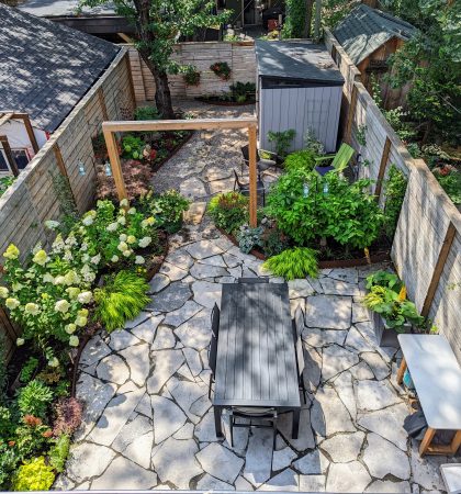 A lush and vibrant garden designed and maintained by Earth and Sole Ltd, featuring a variety of colorful flowers and greenery, including roses, hydrangeas, and hostas, set against a backdrop of natural stone landscaping and a wooden pergola.